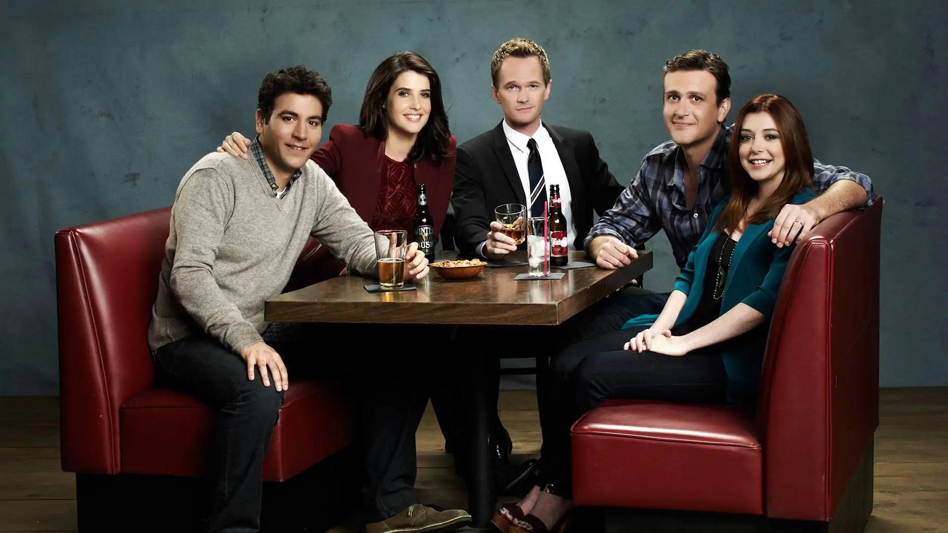 Copertina serie tv How I Met Your Mother con 5 protagonisti seduti a bere su divani rossi